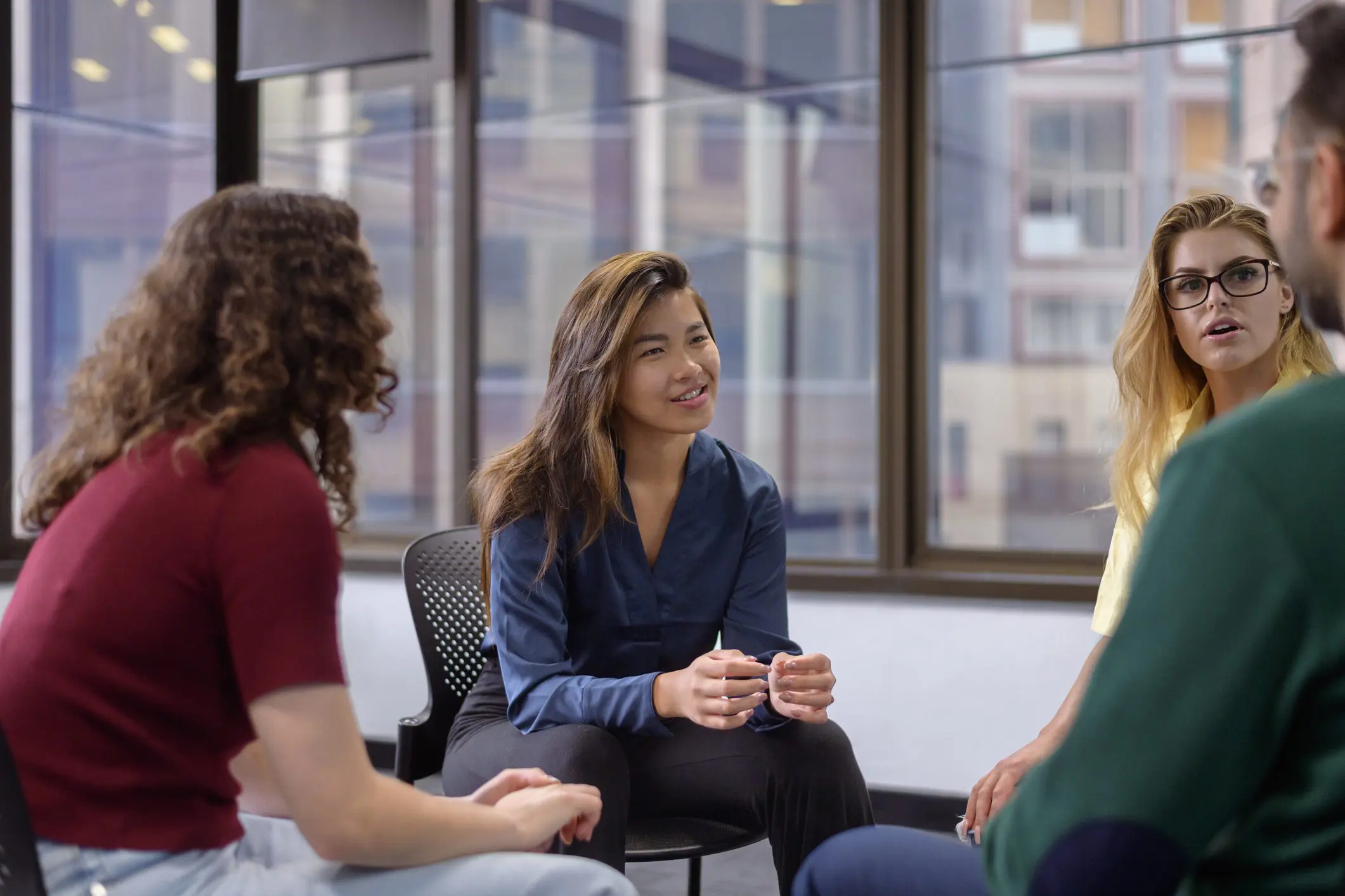 A group of adults sit in a circular formation in outpatient group therapy