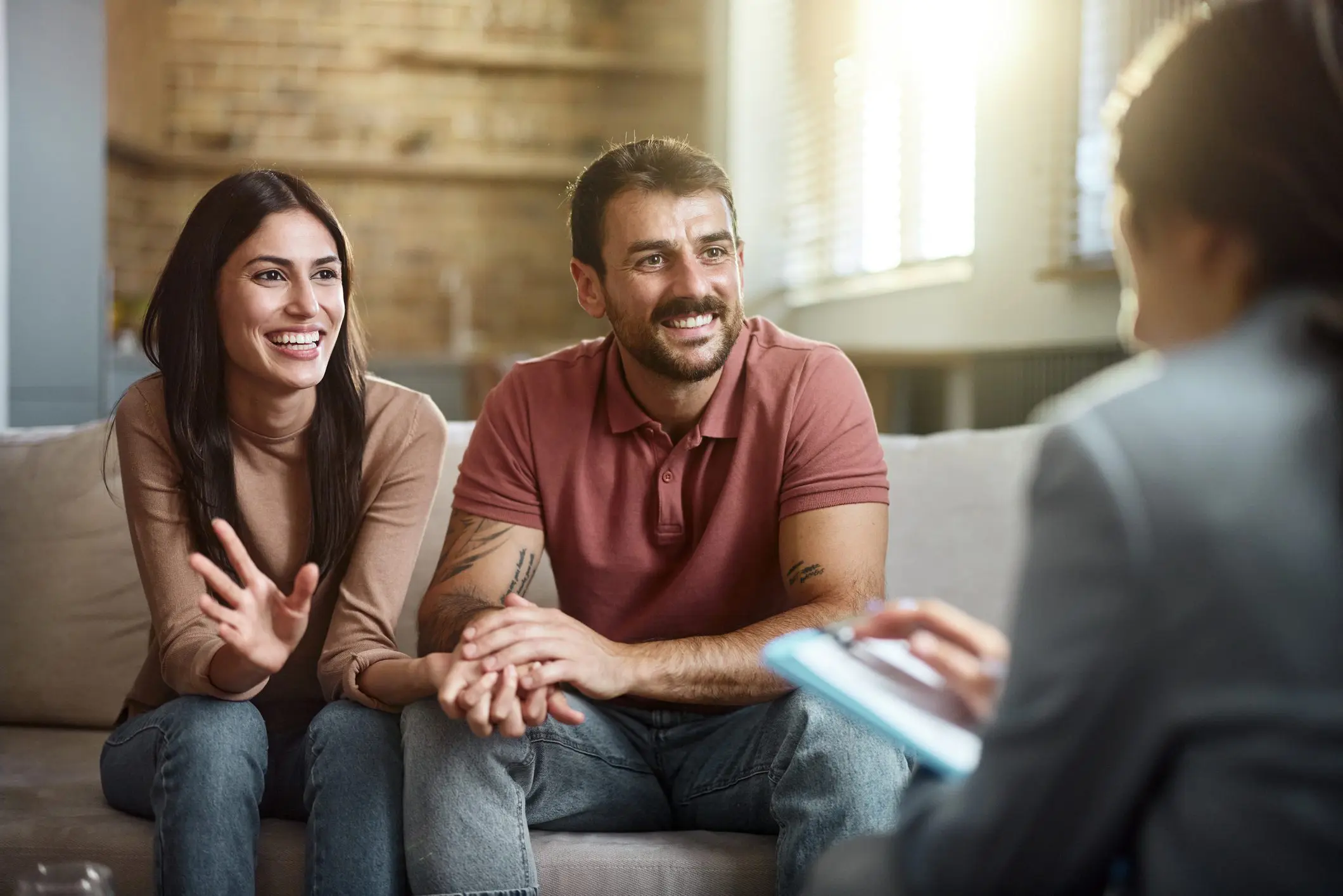 a happy couple sits on a sofa while listening to their therapist