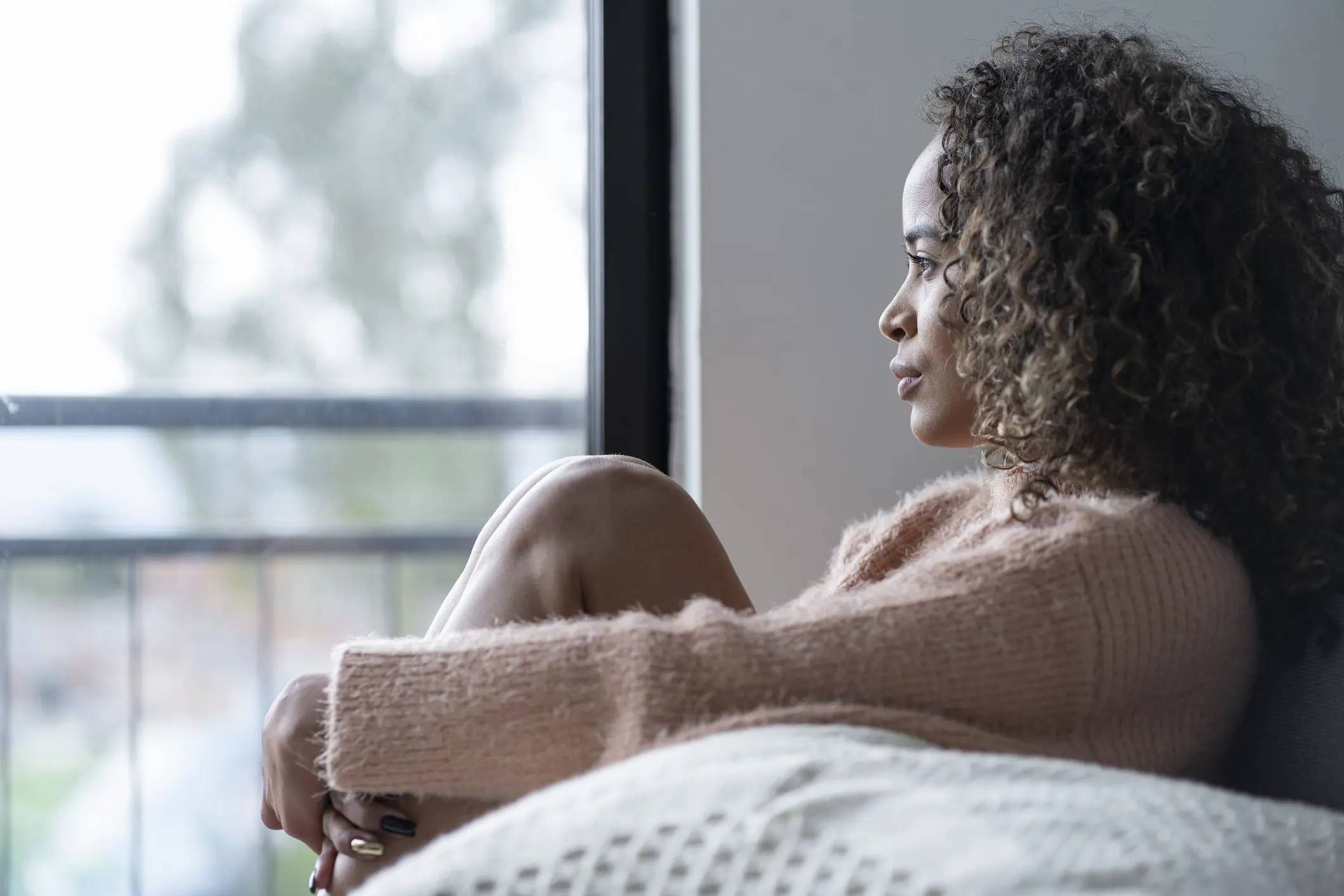 A woman sits in her bedroom alone.
